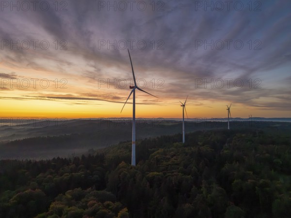 Wind turbines stand in a wooded landscape under a pastel-coloured sky at sunrise, near Schorndorf, Remstal, Rems-Murr-Kreis, Baden-Württemberg, Germany
