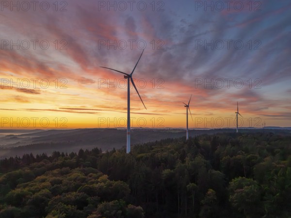 Wind turbines in the foreground of an intense pink-orange sunrise over a forest, near Schorndorf, Remstal, Rems-Murr-Kreis, Baden-Württemberg, Germany