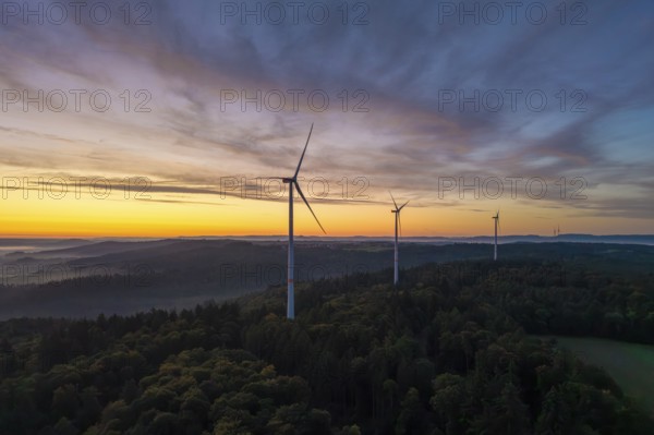 Three wind turbines on a wooded hill with a dramatic sunrise sky, near Schorndorf, Remstal, Rems-Murr-Kreis, Baden-Württemberg, Germany