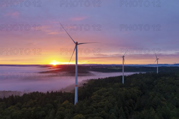 Wind turbines stand high above a misty forest illuminated by an impressive sunrise, near Schorndorf, Remstal, Rems-Murr-Kreis, Baden-Württemberg, Germany