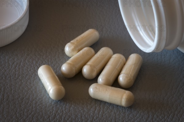 Six beige capsules lie near an open bottle on a dark surface, food supplement, iron supplement, vitamin supplement