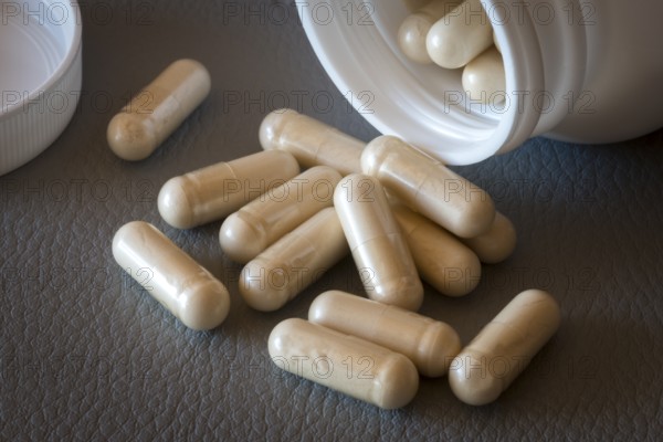 Several beige capsules scattered from an open bottle on a surface, food supplement, iron supplement, vitamin supplement