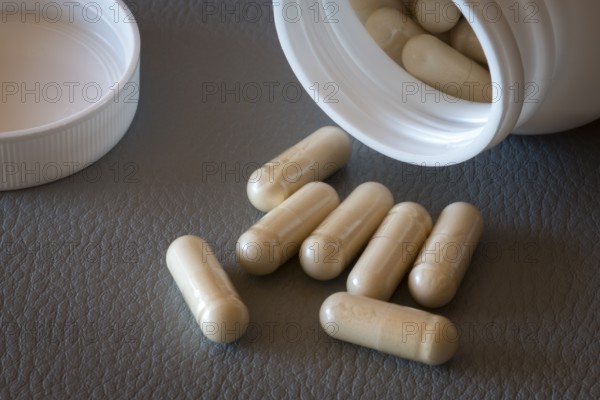 Open bottle with beige capsules and separate lid on one surface, food supplement, iron supplement, vitamin supplement