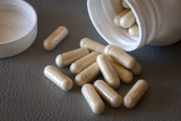 Various beige capsules taken from a half-opened bottle, food supplement, iron supplement, vitamin supplement