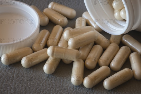 Close-up of beige capsules rolling out of an open bottle onto a surface, food supplement, iron supplement, vitamin supplement