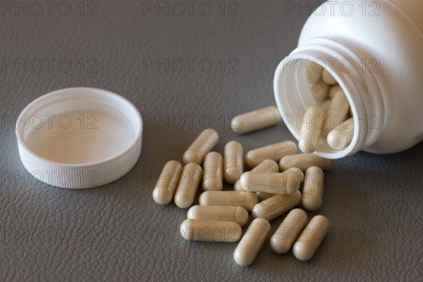 Open bottle with scattered beige capsules on a dark surface, food supplement, iron preparation, vitamin preparation