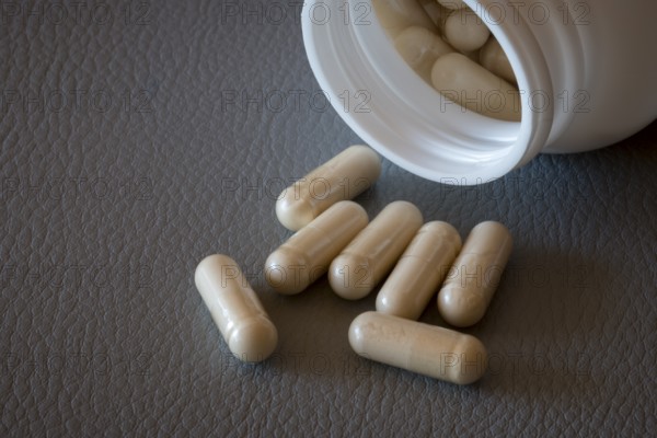 Partially emptied bottle with beige capsules on a textured surface, food supplement, iron supplement, vitamin supplement