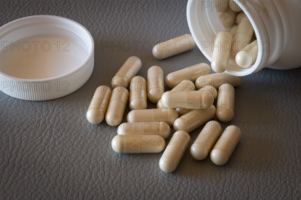 Beige capsules that have fallen from an open bottle with the lid removed onto a surface, food supplement, iron supplement, vitamin supplement