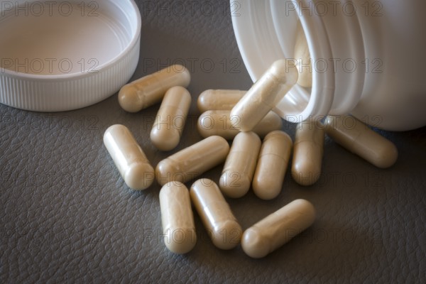 Beige capsules lying on a textured surface from an opened bottle, food supplement, iron supplement, vitamin supplement