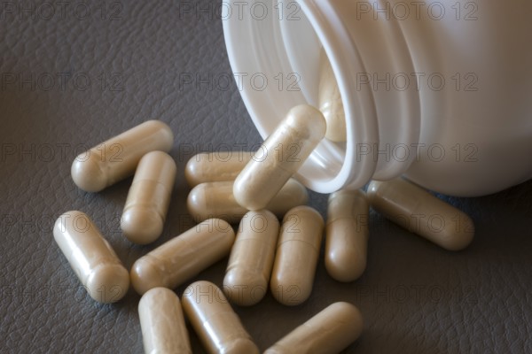 Beige capsules roll out of an open bottle onto a dark surface, food supplement, iron supplement, vitamin supplement