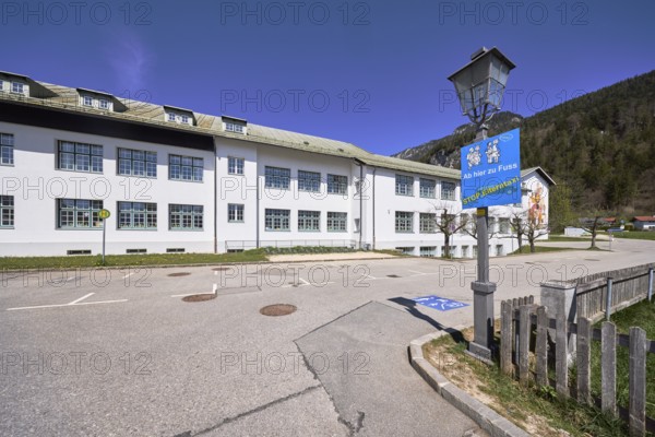 Primary and secondary school Bischofswiesen, sign Stop parent taxi, building, lantern, bus stop, problem parent taxi, wooden fence, hill, coniferous forest, blue sky, cirrostratus clouds, intersection Göllstraße with Schulstraße, Bischofswiesen, district Berchtesgadener Land, Bavaria, Germany