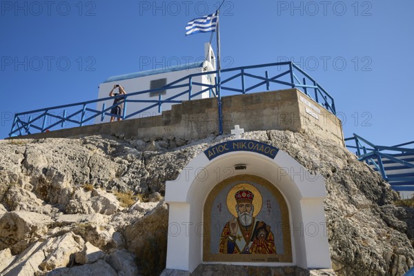 Chapel in rock formation with icon and Greek flag in the foreground, Chapel of Agios Nikolaos, harbour, Kolymbia, Rhodes, Dodecanese, Greek Islands, Greece