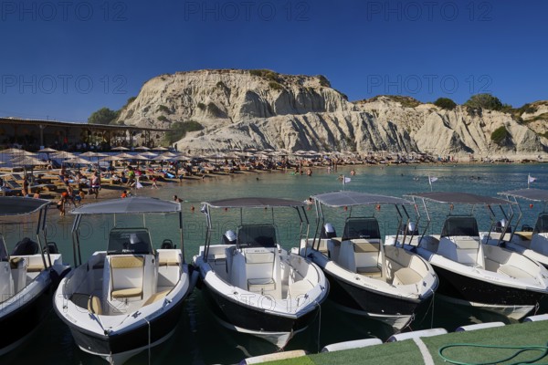 Boats in front of a rocky beach section with holiday atmosphere, many bathers and sunshades visible, Limanaki beach, sandstone rocks, Kolymbia, Rhodes, Dodecanese, Greek Islands, Greece