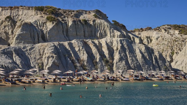 Beach in front of a large rock face, lined with sun loungers and umbrellas, bathers enjoying the sea, Limanaki beach, sandstone cliffs, Kolymbia, Rhodes, Dodecanese, Greek Islands, Greece