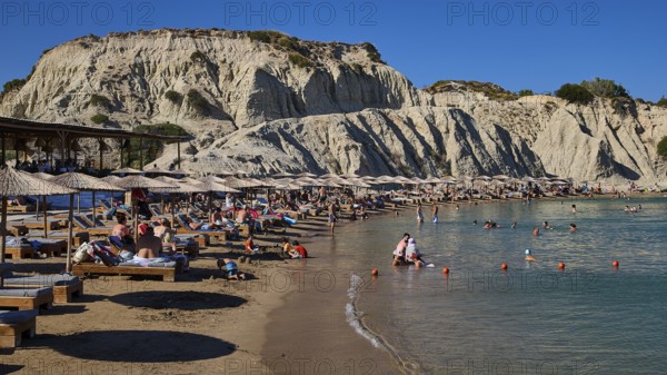 Long beach with sun loungers and bathers in front of an impressive rock face, Limanaki beach, sandstone cliffs, Kolymbia, Rhodes, Dodecanese, Greek Islands, Greece