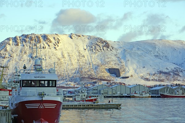 Norwegian harbour in front of snowy mountains in winter with boats and clouds in the sky, Myre, Vesteralen, Nordland, Arctic, Norway