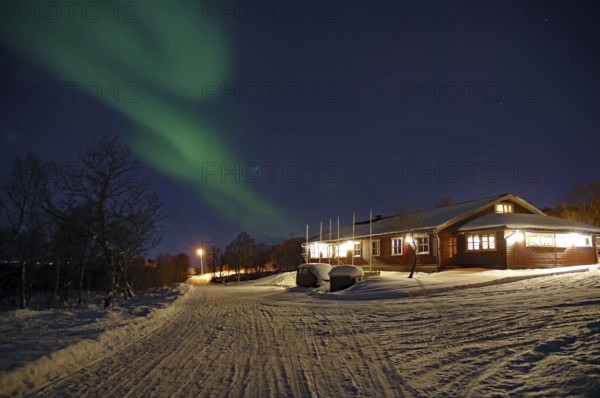 A snowy path leads to a house under the Northern Lights and a clear night sky, Sortland campsite, Vesteralen, Nordland, Arctic, Norway