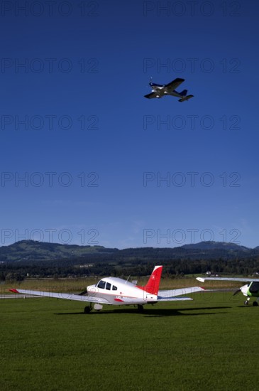 BRM Aero Bristell B23 identification aircraft registration HB-KGU taking off over Piper Archer II HB-PPY on the ground, Wangen-Lachen airfield, LSPV, Canton Schwyz, Switzerland