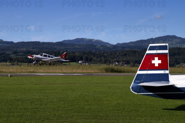 Piper Archer II with the registration HB-PPY on take-off, tail unit of a Mooney M20J 200 HP HB-DGW on the ground, Wangen-Lachen airfield, LSPV, Canton Schwyz, Switzerland
