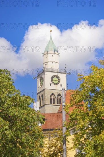 Church tower with clock rises above trees under a blue sky with clouds, Lake Constance, Germany