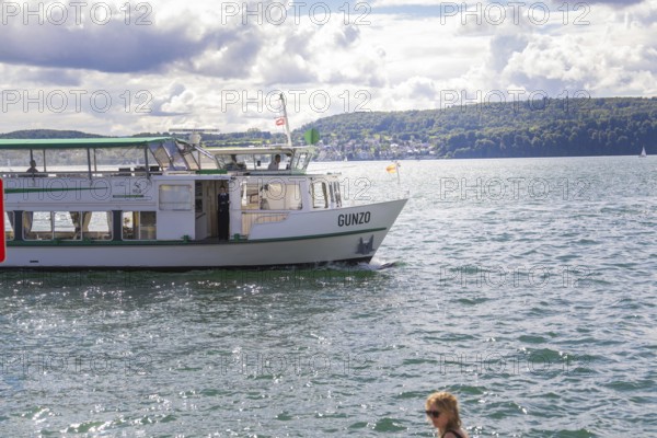 Small ship sailing on a lake with urban shore in the background, Lake Constance, Germany