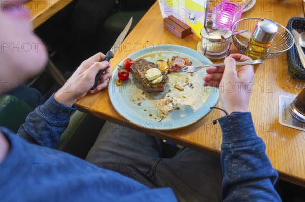 Person eating a dish in a restaurant, consisting of meat and tomatoes on a plate, Lake Constance, Germany