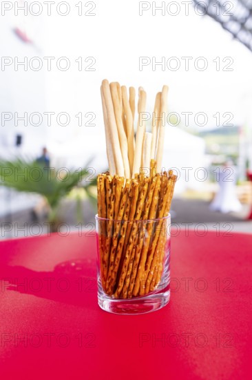 A glass container with breadsticks stands on a red table in an outdoor event area, Lake Constance, Germany