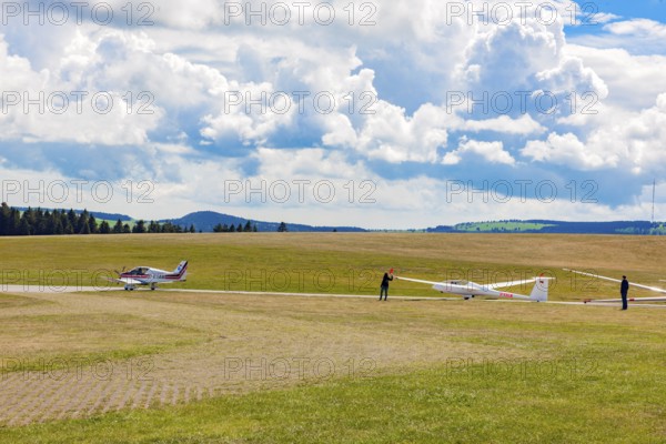 View of left single-engine light aircraft Robin DR400 as tow plane for right glider Glider pilots standing on runway of Wasserkuppe airfield, Gersfeld, district of Fulda, Hesse, Germany, just in front of take-off