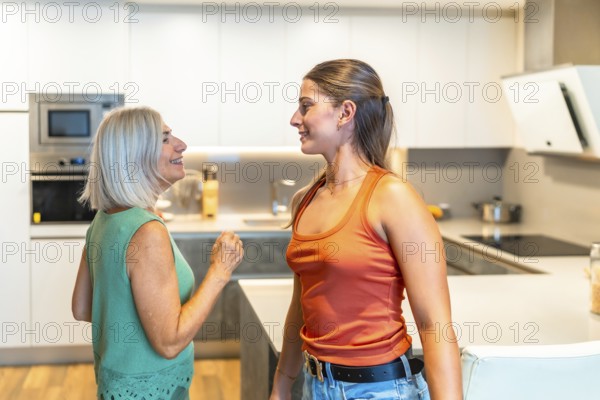 Senior woman and young adult sharing a lighthearted moment, gesturing and smiling in a modern kitchen, enjoying family time