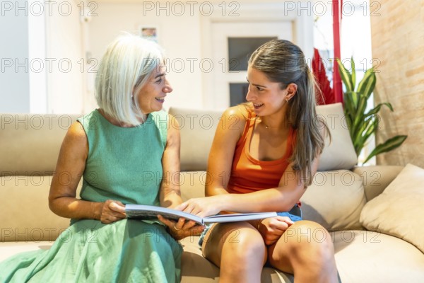 Smiling senior woman and young woman reading a book together on a comfortable sofa in the living room, enjoying quality time