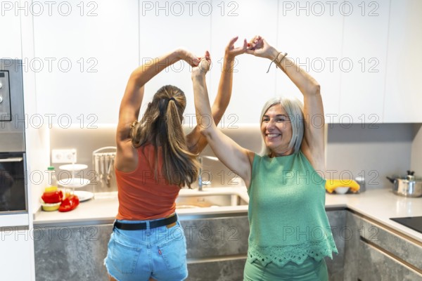 Two women joyfully dancing in a modern kitchen, embodying happiness and togetherness, surrounded by fresh ingredients and bright decor