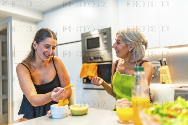 Two women, one older and one younger, enjoying healthy snacks together in a modern kitchen, highlighting family bonding and healthy living