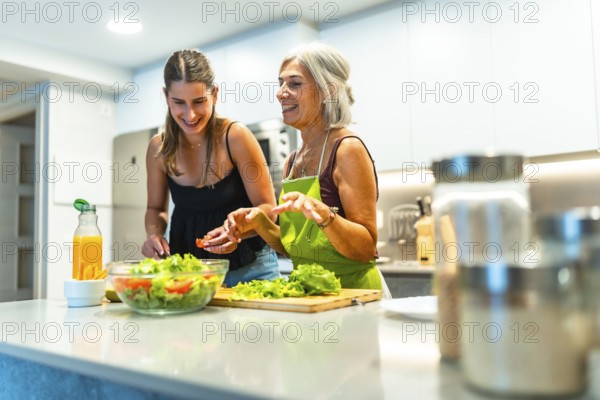 Older and younger women enjoying time in a modern kitchen, preparing a fresh salad. Laughter and joy highlight their shared culinary experience