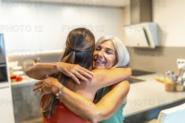 Happy senior woman embracing her adult daughter in a kitchen, enjoying a tender moment of affection and family connection