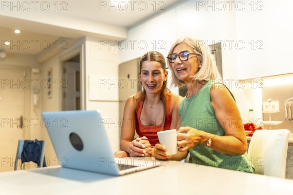 Happy senior woman and her daughter are drinking coffee and having a video call on a laptop in a modern kitchen