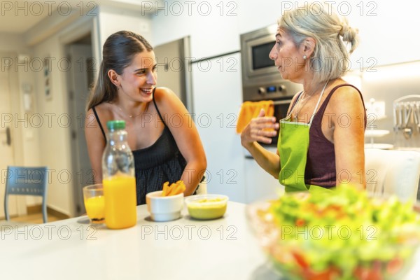 Senior woman wearing apron explaining recipe to her young adult daughter while preparing a healthy meal together in a modern kitchen