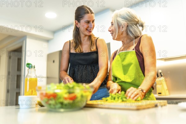Two women happily preparing a colorful vegetable salad in a modern kitchen, enjoying conversation and bonding over healthy cooking