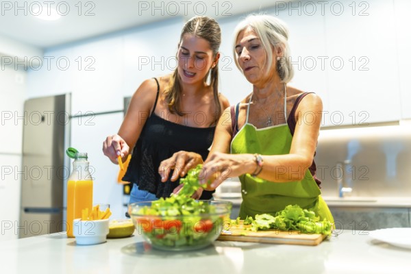 Mother and daughter preparing a mixed salad with lettuce, tomato, and orange juice in a modern kitchen, enjoying time together and promoting healthy eating habits