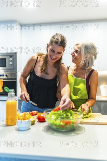 Elderly woman and young adult preparing a fresh salad together, showcasing family connection and healthy lifestyle in a bright kitchen