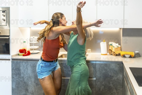 Happy mother and daughter are dancing together in their modern kitchen, enjoying a carefree moment of joy and bonding