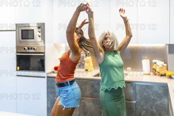 Two women enjoy a lively dance in a contemporary kitchen, celebrating happiness and friendship with joyful expressions and energetic movements