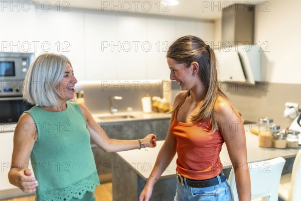 Senior mother and adult daughter having fun dancing together in a bright modern kitchen, enjoying family time