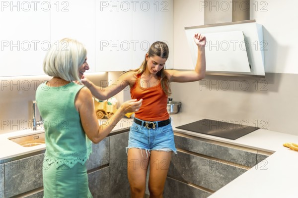 Happy mother and daughter are dancing and having fun while cooking together in a modern kitchen