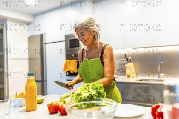 Happy mature woman wearing an apron, preparing a fresh vegetable salad in a modern kitchen filled with vibrant colors and healthy ingredients