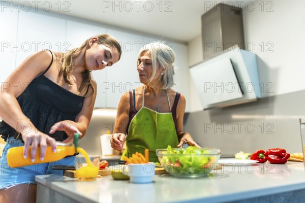 Two women preparing a healthy meal in a contemporary kitchen, focusing on fresh ingredients like salad and orange juice, promoting family bonding