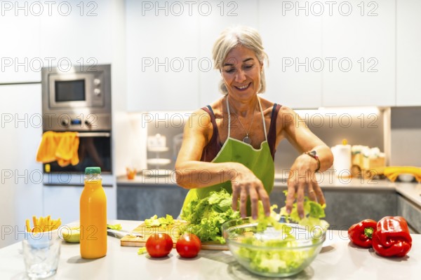 Elderly woman wearing an apron, making a salad with fresh ingredients in a bright kitchen, showcasing healthy lifestyle and cooking at home