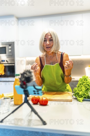Cheerful mature food blogger engaging with her audience while recording a video tutorial on preparing nutritious meals in her cozy kitchen