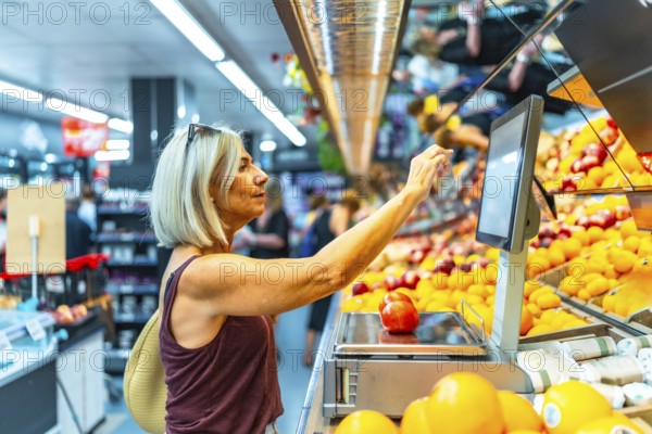 Senior woman using a digital weight scale to weigh fresh fruits at the supermarket, selecting her groceries for a healthy diet