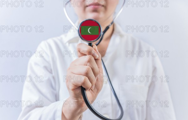 Female doctor holding stethoscope with Maldives flag. National health system of Maldives