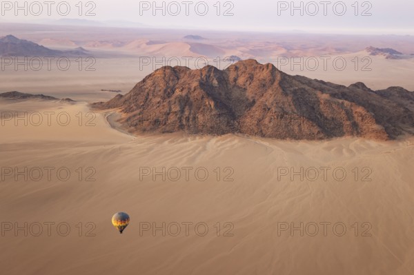 The hot-air balloon above an arid plain and isolated mountain ridges at the edge of the Namib Desert. Aerial view from a second balloon. Namibia